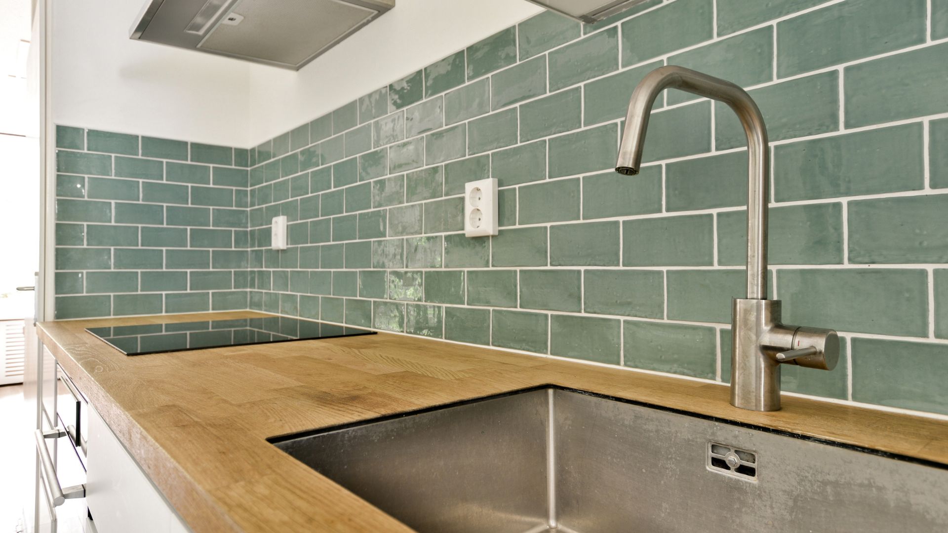 Modern kitchen with green subway tiles, wooden countertop, and stainless steel sink
