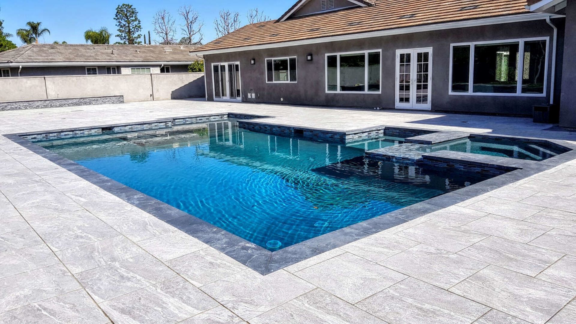 Modern backyard with blue swimming pool and gray stone patio