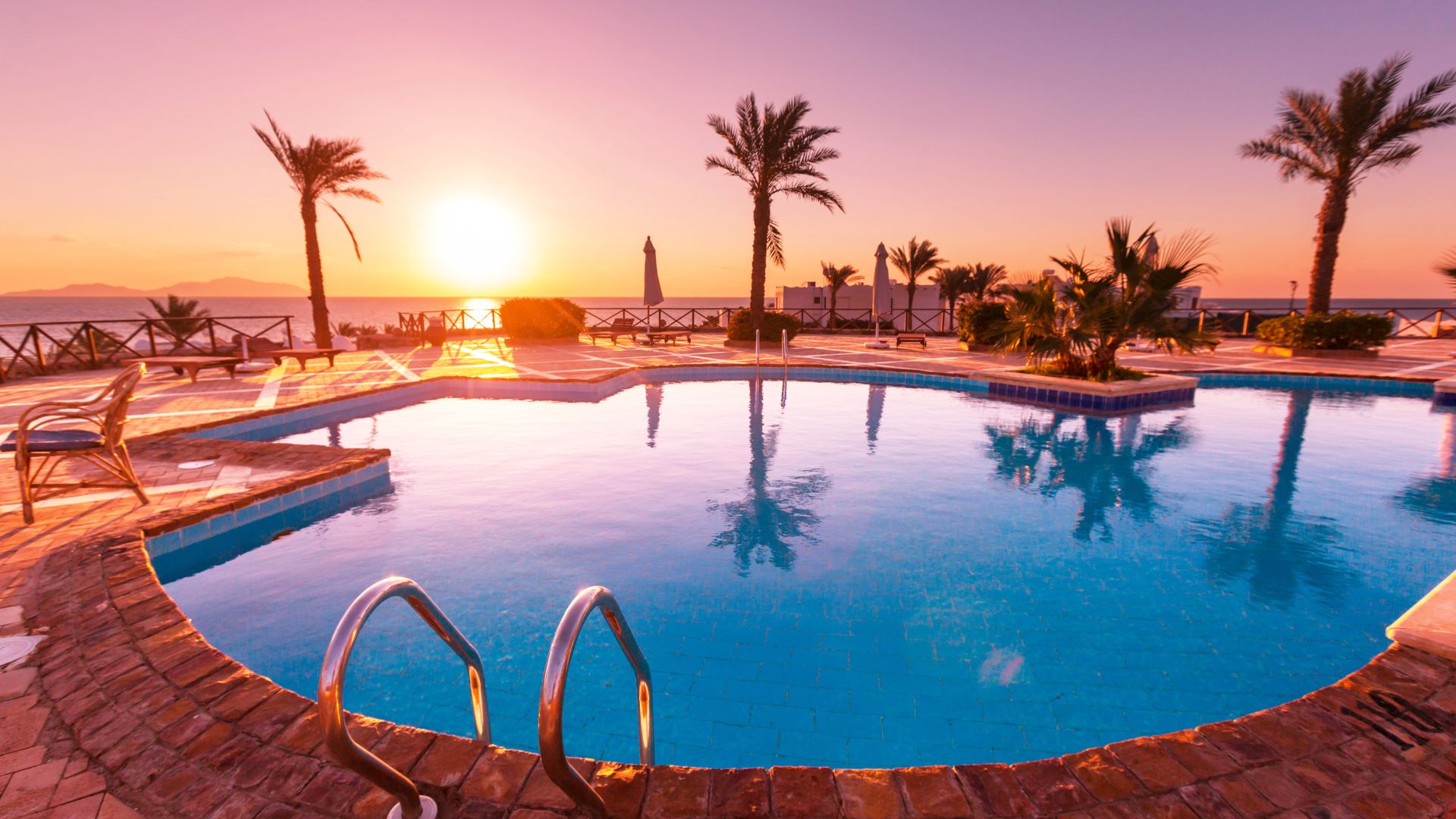 Sunset over tropical resort swimming pool with palm trees and ocean view