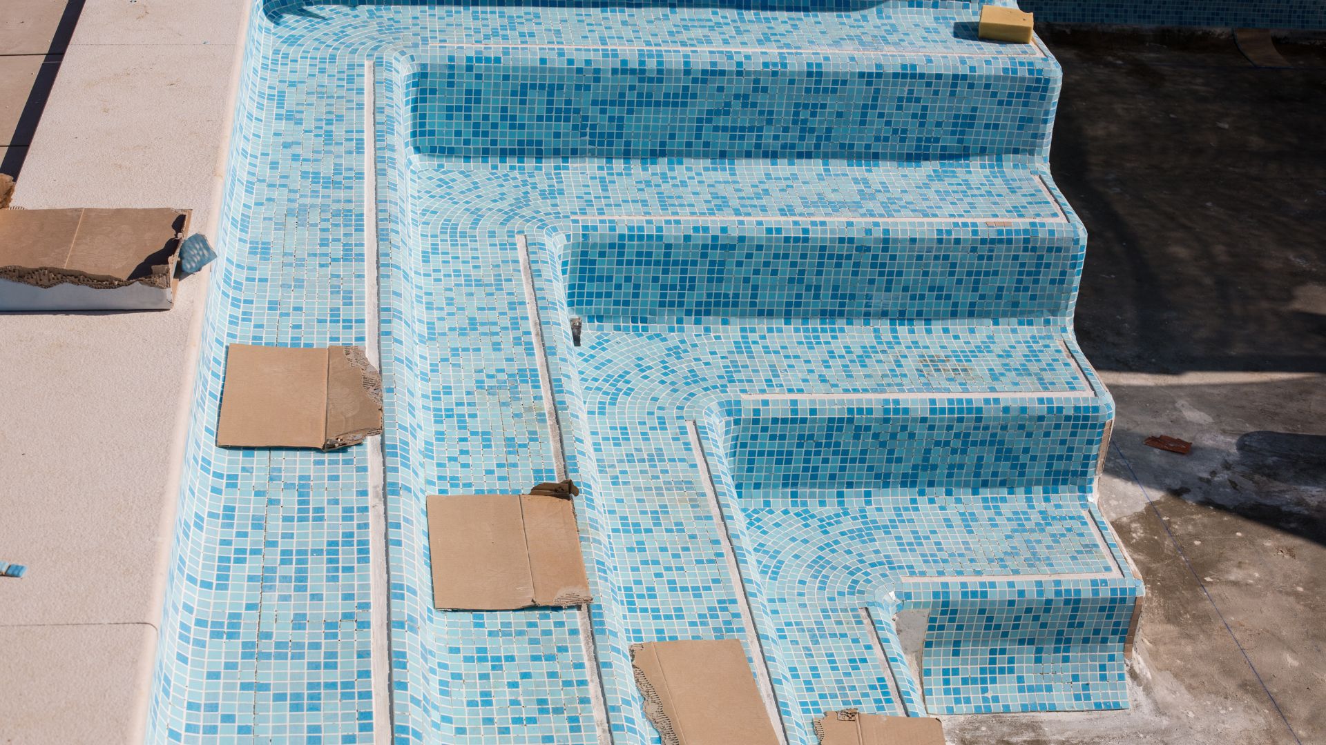 Blue mosaic pool steps with construction materials during tiling process