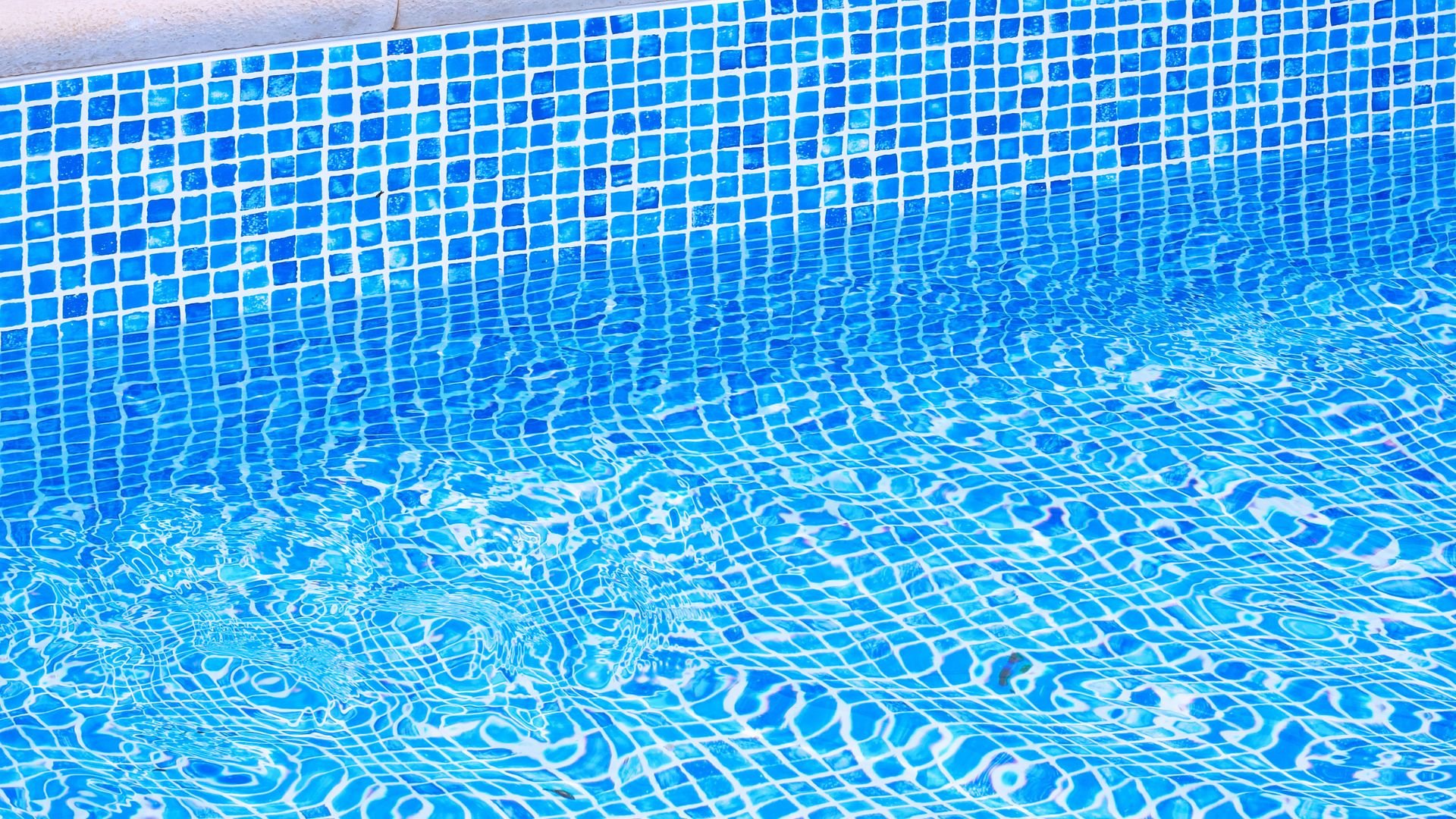 Blue swimming pool tiles with rippling water creating geometric patterns