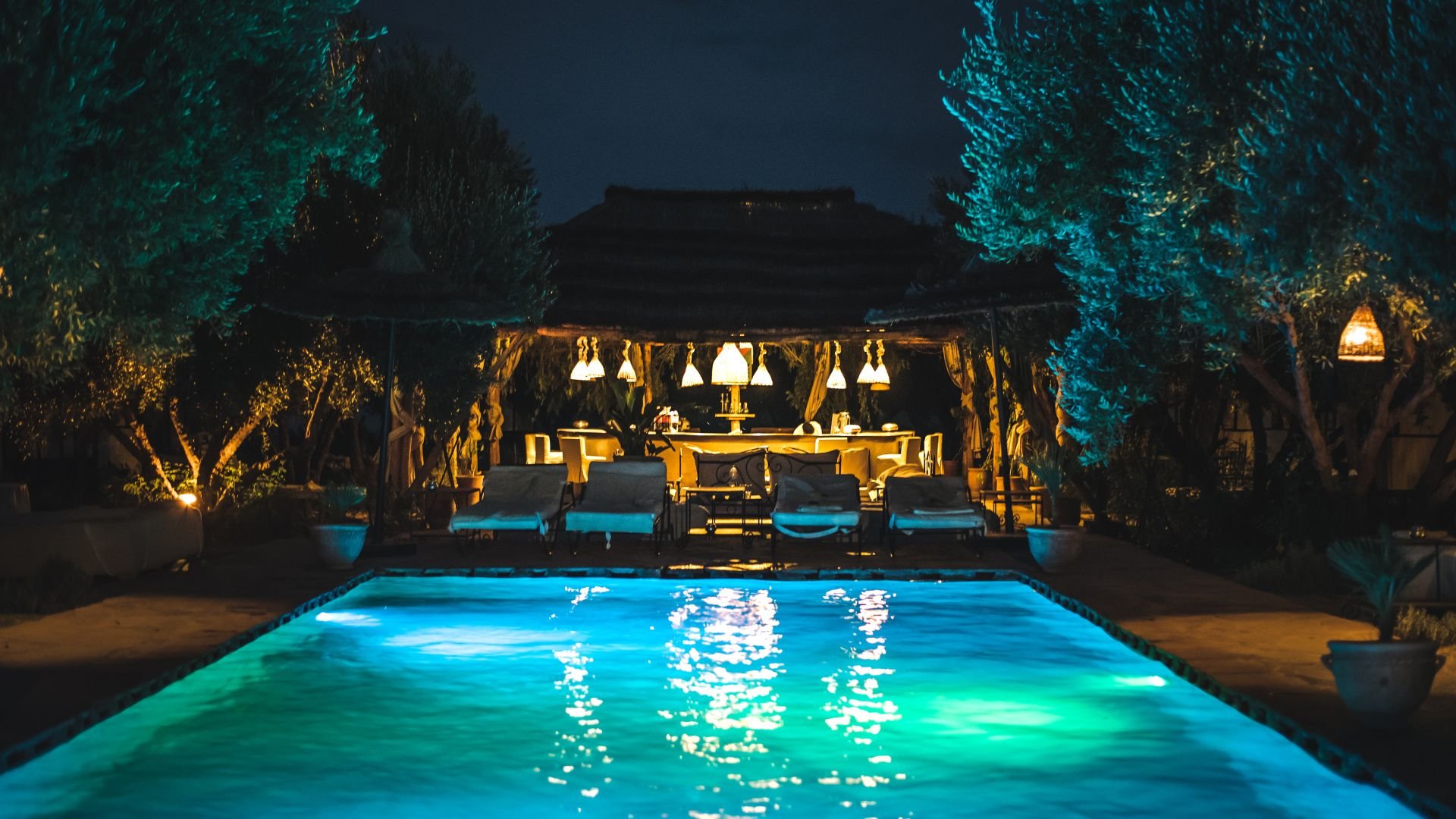 Illuminated swimming pool with glowing blue water and cozy outdoor seating area