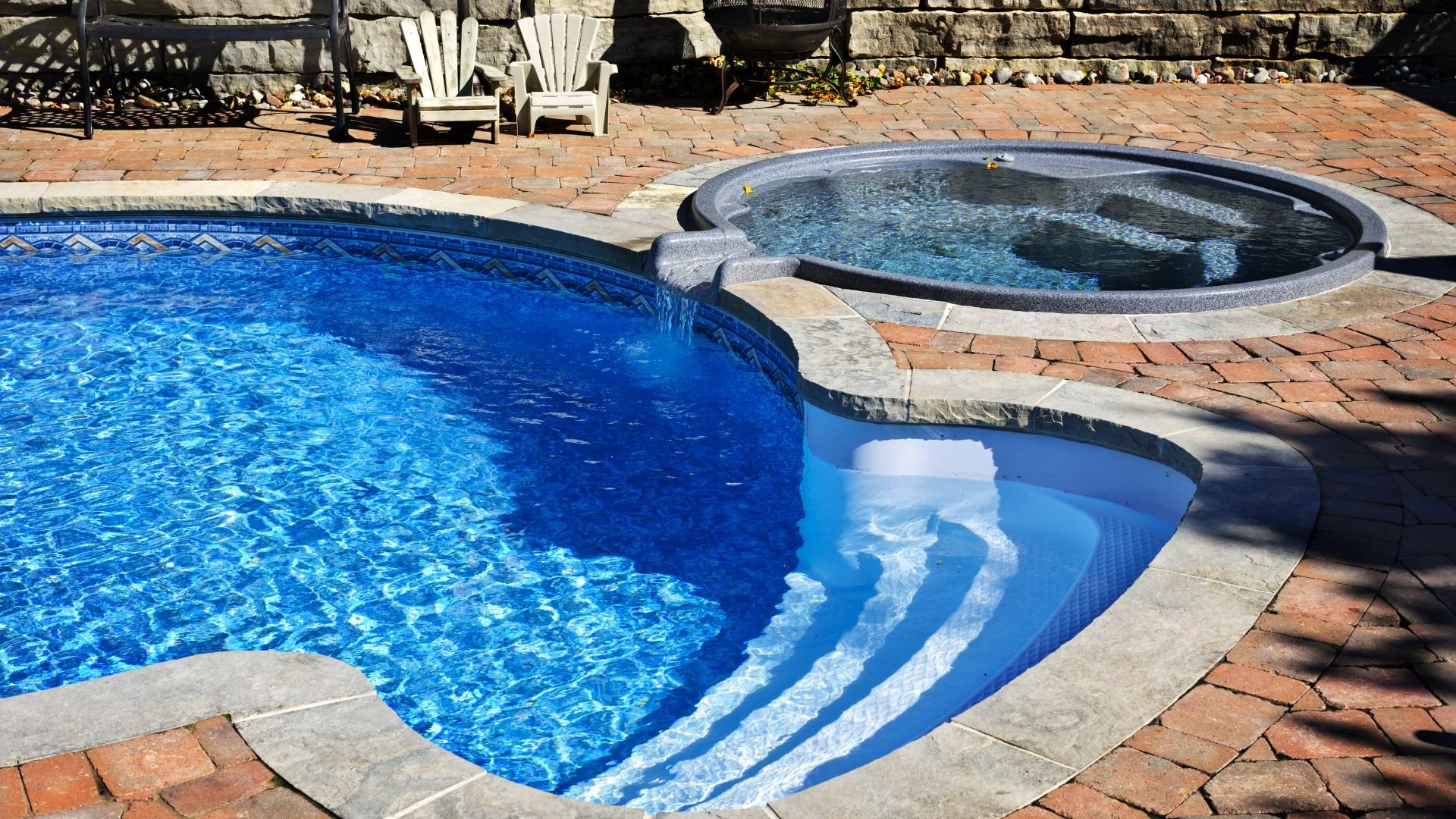 Backyard swimming pool with curved blue water and attached round hot tub
