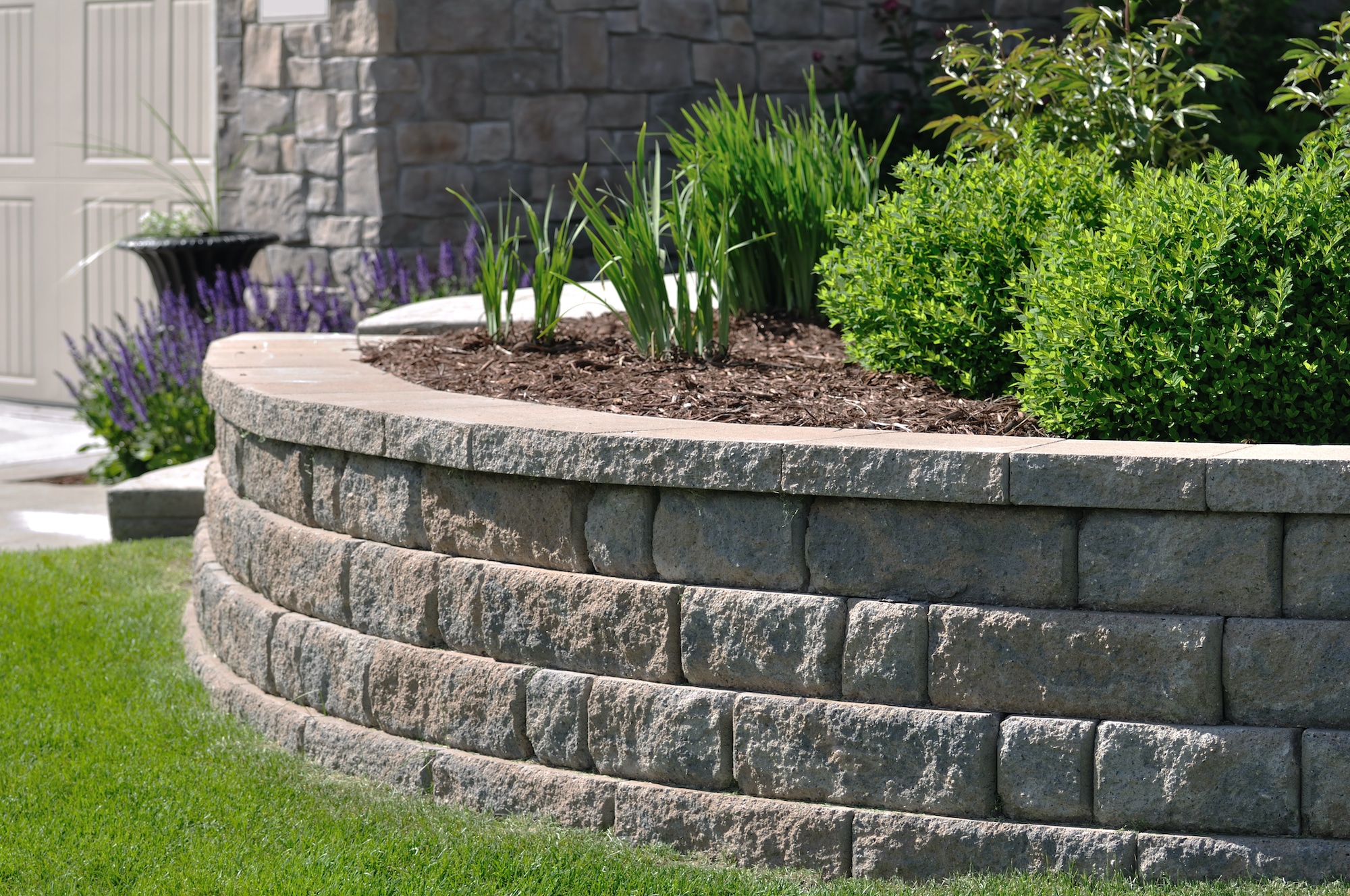 Curved stone retaining wall with plants and mulch in landscaped garden